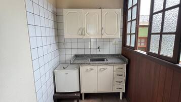 Een kleine keuken met witte kastjes, een spoelbak en een raam.
