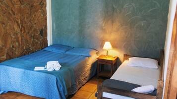 A room with two beds, a stone wall, a ceiling fan, and a tiled floor.