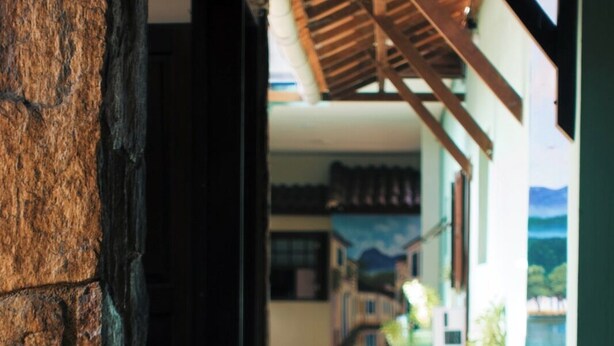 A stone archway leading to a covered outdoor area with a wooden ceiling and a view of a building with a mural. - Pousada Pouso de ícaro (Paraty)