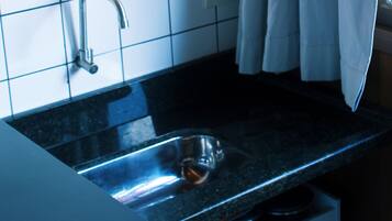 Een keuken met een spoelbak van roestvrij staal, een kraan en een raam met gordijn.