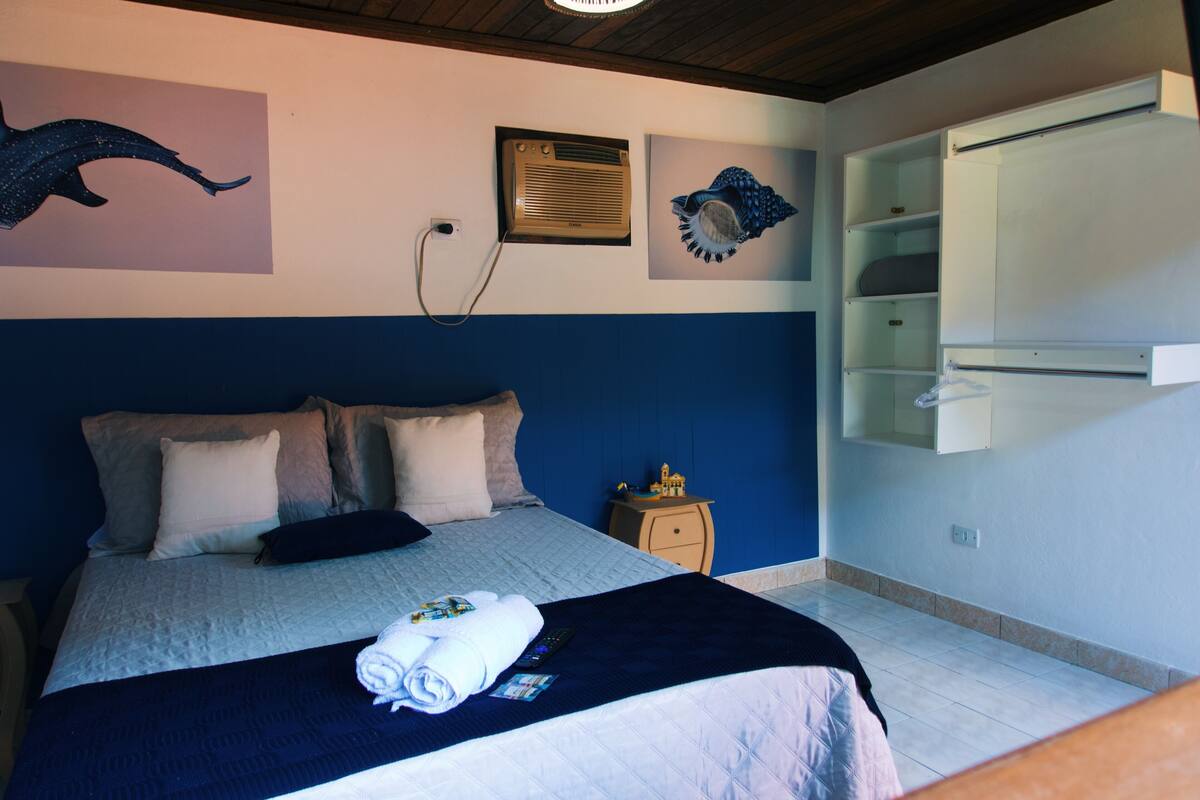 Una habitación de hotel con cama, mesita de noche, aire acondicionado de pared y estante empotrado.