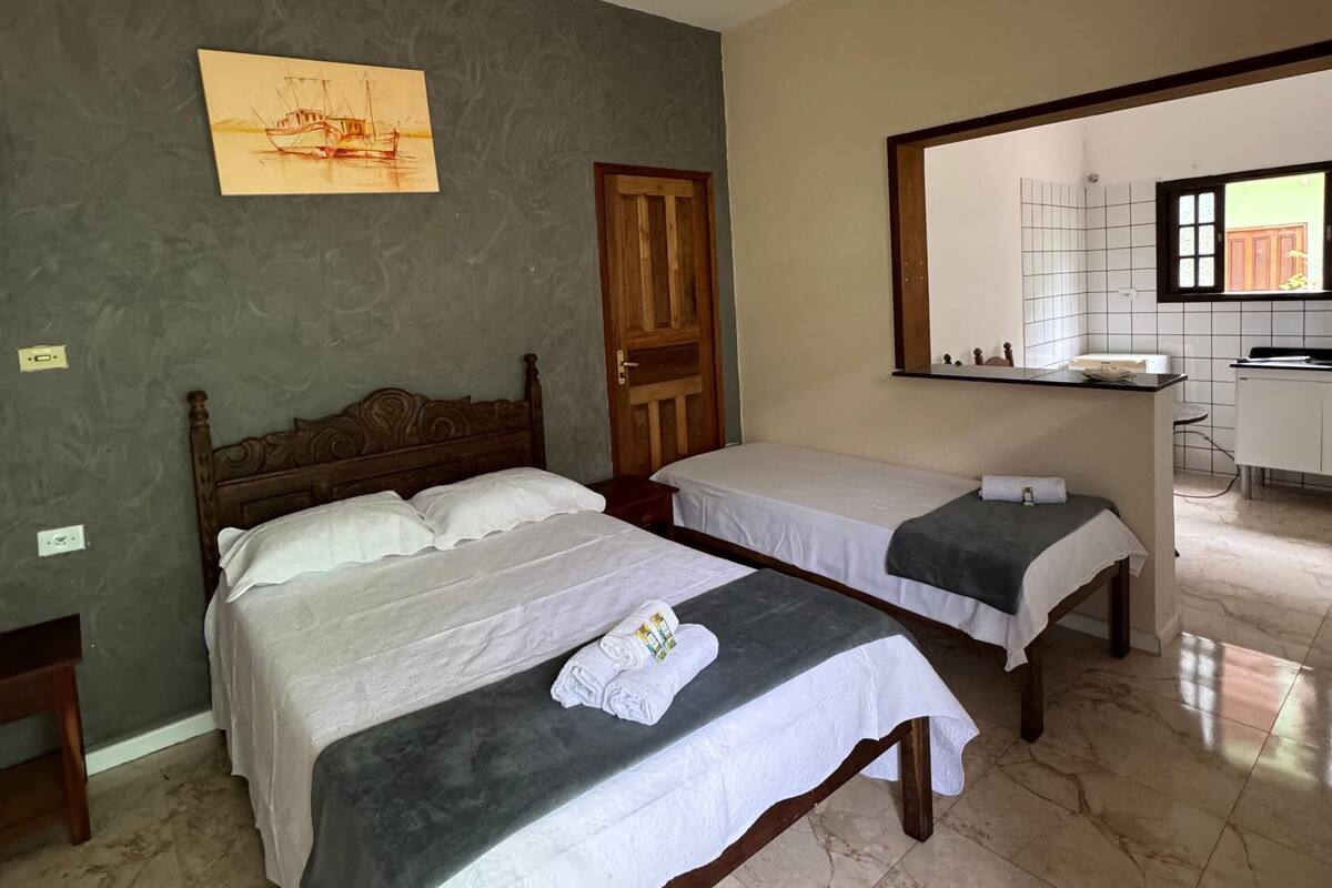 Habitación de hotel con dos camas, un ventilador de techo, un cuadro, una puerta de madera y vistas a la cocina a través de un vano abierto.