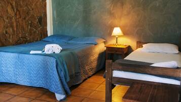 Una habitación con dos camas, una pared de piedra, suelo de madera y una mesita de noche con lámpara.