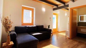 A spacious living area with a wooden ceiling, a dark-colored sofa, a small table with a vase, and a wooden floor. - Detached house on three levels with garden, a stone's throw from the center of Teglio (Teglio)