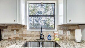 Una cocina con encimera de granito, pileta de acero inoxidable y ventana con vista a árboles.