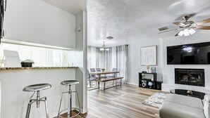 Una sala de estar moderna con chimenea, un comedor con mesa y sillas, y una zona de cocina con taburetes de bar.
