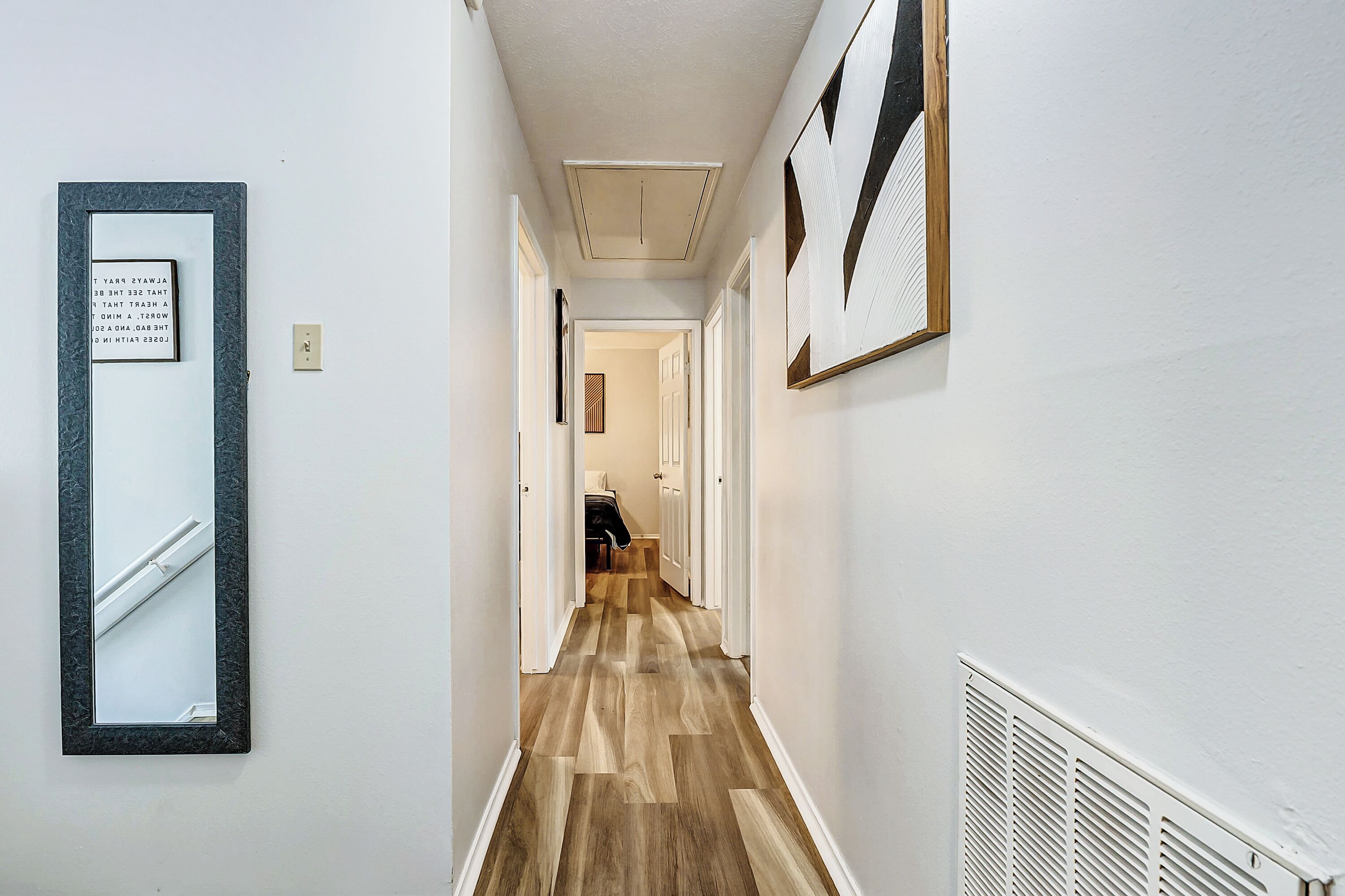 Un couloir doté d’un plancher en bois, de murs blancs et d’un luminaire au plafond.