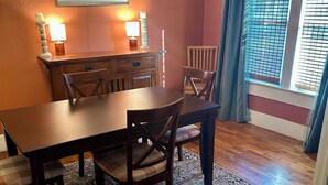 Un espace repas comprenant une table et des chaises en bois, un tapis à motifs et des œuvres d’art décoratives accrochées au mur.