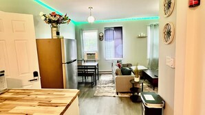 A modern kitchen with a wooden countertop, a dining area with a table and chairs, a living room with a sofa and a coffee table, and a hallway with a trash bin.