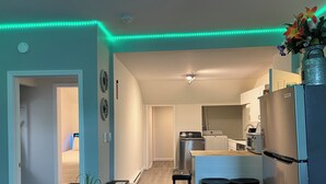 A compact kitchen with modern appliances, a dining area with stools, and a hallway leading to a bedroom.