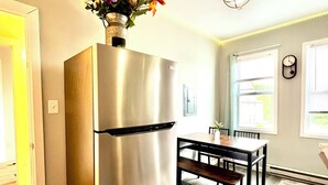 A kitchen with a stainless steel refrigerator, a dining table with chairs, and a wooden floor.