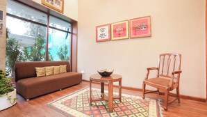 Una sala de estar con un sofá marrón, una silla de madera, una mesita redonda con un cuenco, una alfombra estampada y tres cuadros en la pared.