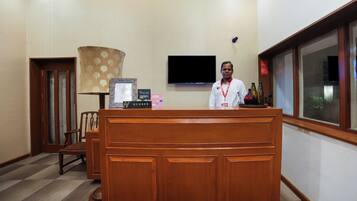 A reception desk with a nameplate, a television mounted on the wall, and a window with blinds.