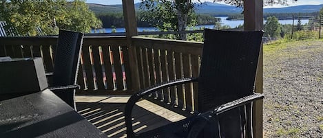A covered outdoor seating area with a table and chairs, overlooking a lake and forested hills.