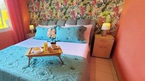 Een slaapkamer met bloemenbehang, een bed met een blauwe quilt, een dienblad met ontbijtartikelen en een nachtkastje met een lamp.