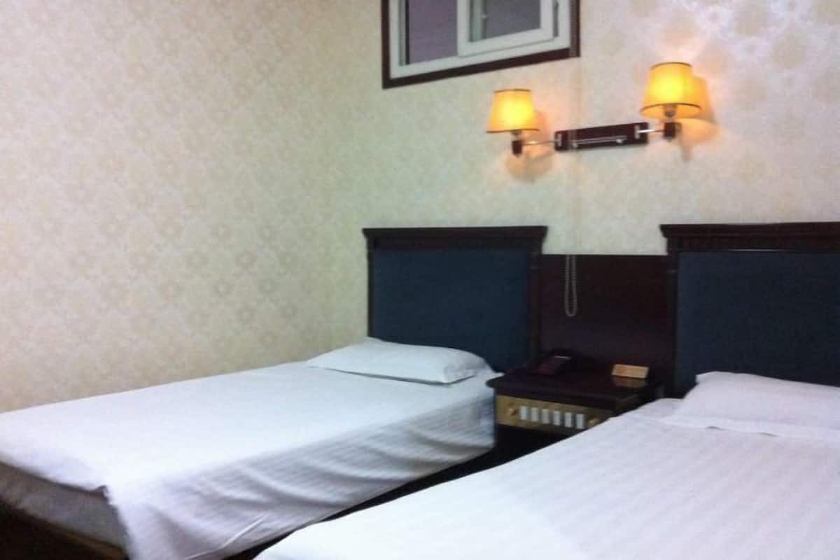 Ett hotellrum med två separata sängar, ett nattduksbord med en telefon och väggmonterade lampor.
