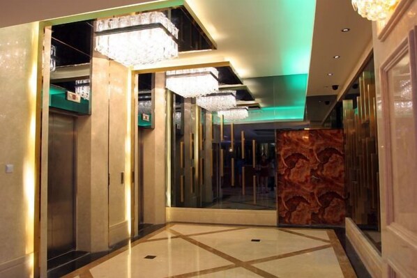 Un pasillo de hotel con un muro espejado, un candelabro y un papel tapiz decorado.