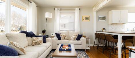 A modern living room with a sofa, coffee table, and a dining area with bar stools.