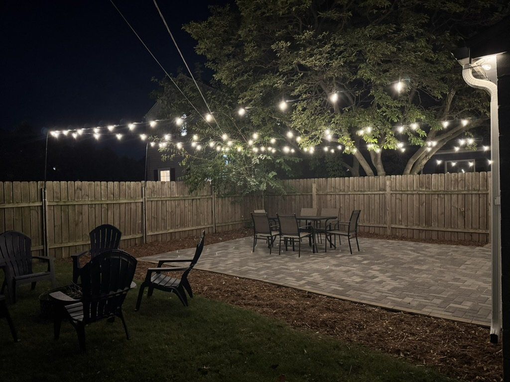 Un patio al aire libre con cerramiento de madera, luces colgantes y mobiliario exterior.
