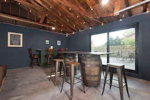 A bar area with wooden stools, a bar counter, and a large window offering a view of the outdoors.