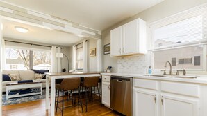 A modern kitchen with white cabinetry, a stainless steel dishwasher, and a large window with blinds. - Rockne Quad<>Updated 3BR 2BA Home 1 Mi to ND (South Bend)