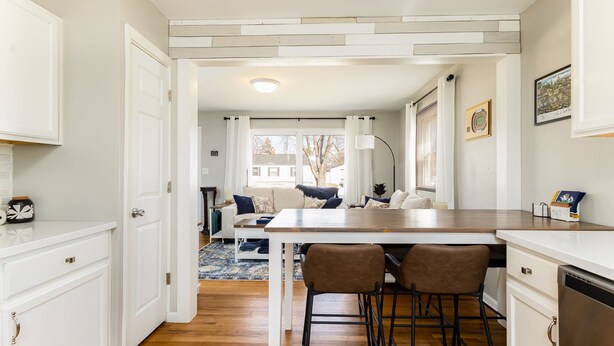 A modern kitchen with white cabinetry, a wooden countertop, and a central island with bar stools. - Rockne Quad<>Updated 3BR 2BA Home 1 Mi to ND (South Bend)