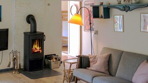 A cozy living room with a wood-burning stove, a sofa, a lamp, and a small table. - 6 Person Holiday Home in Blokhus (Blokhus)