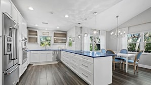 Una cocina moderna con armarios blancos, encimera azul y un comedor con sillas azules.