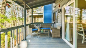 A covered porch with wicker furniture and a table, overlooking a forested area.