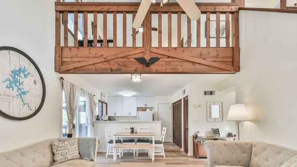 A spacious living room with a high ceiling, a dining area, and a kitchen in the background.