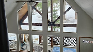 A spacious loft with high ceilings, large windows, and a view of a snowy outdoor deck.