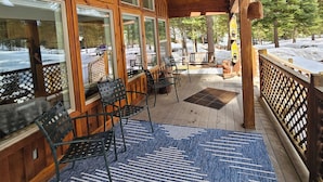 A covered outdoor seating area with large windows, wooden deck, and a blue patterned rug.