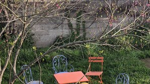 A garden with metal chairs and a table, surrounded by greenery and a stone wall.