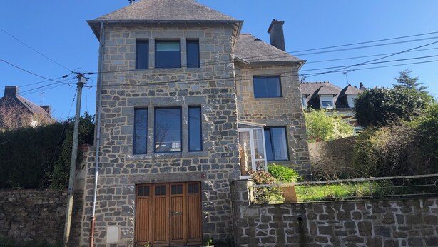 A stone building with a central tower, multiple windows, and a wooden door.