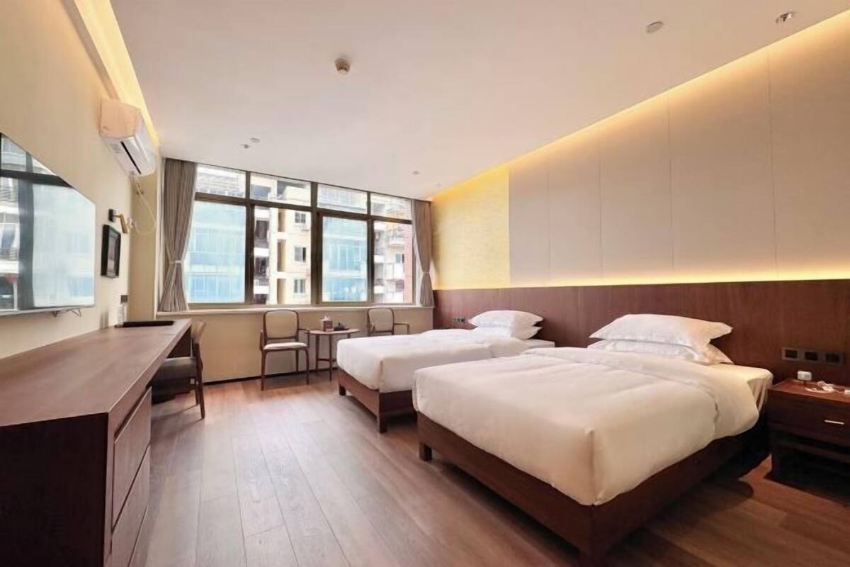 Ein Hotelzimmer mit zwei Betten, einem Schreibtisch und einem Fenster mit Blick auf die Stadt.