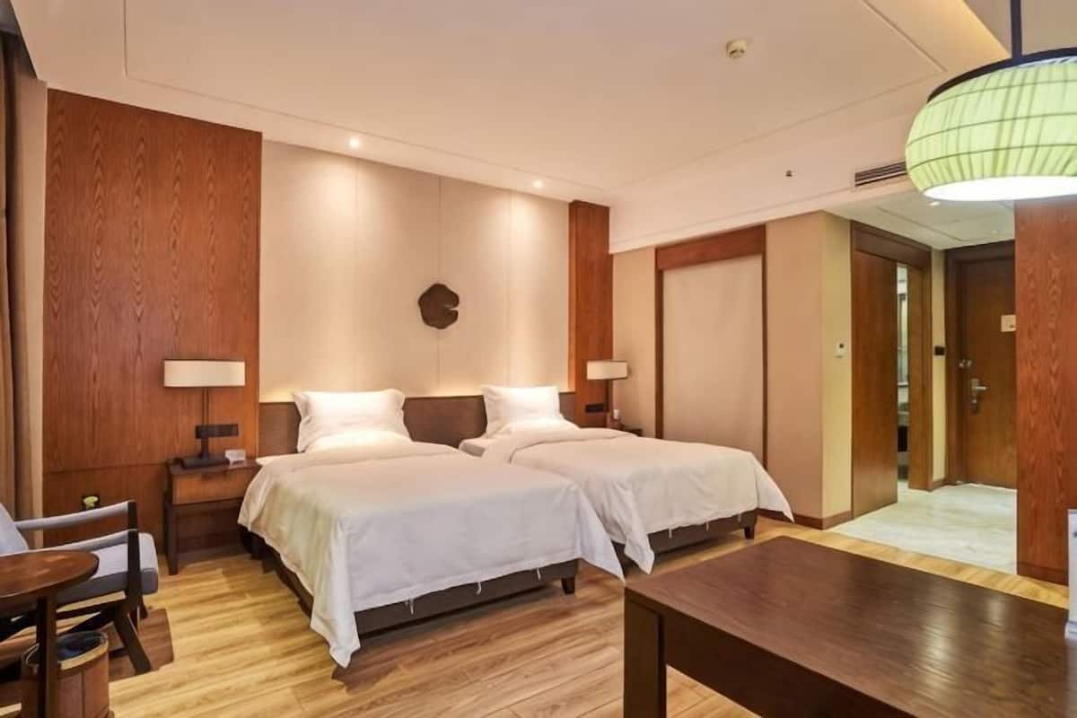 Ein Hotelzimmer mit zwei Betten, Holzboden, einem Schreibtisch und einer Lampe.