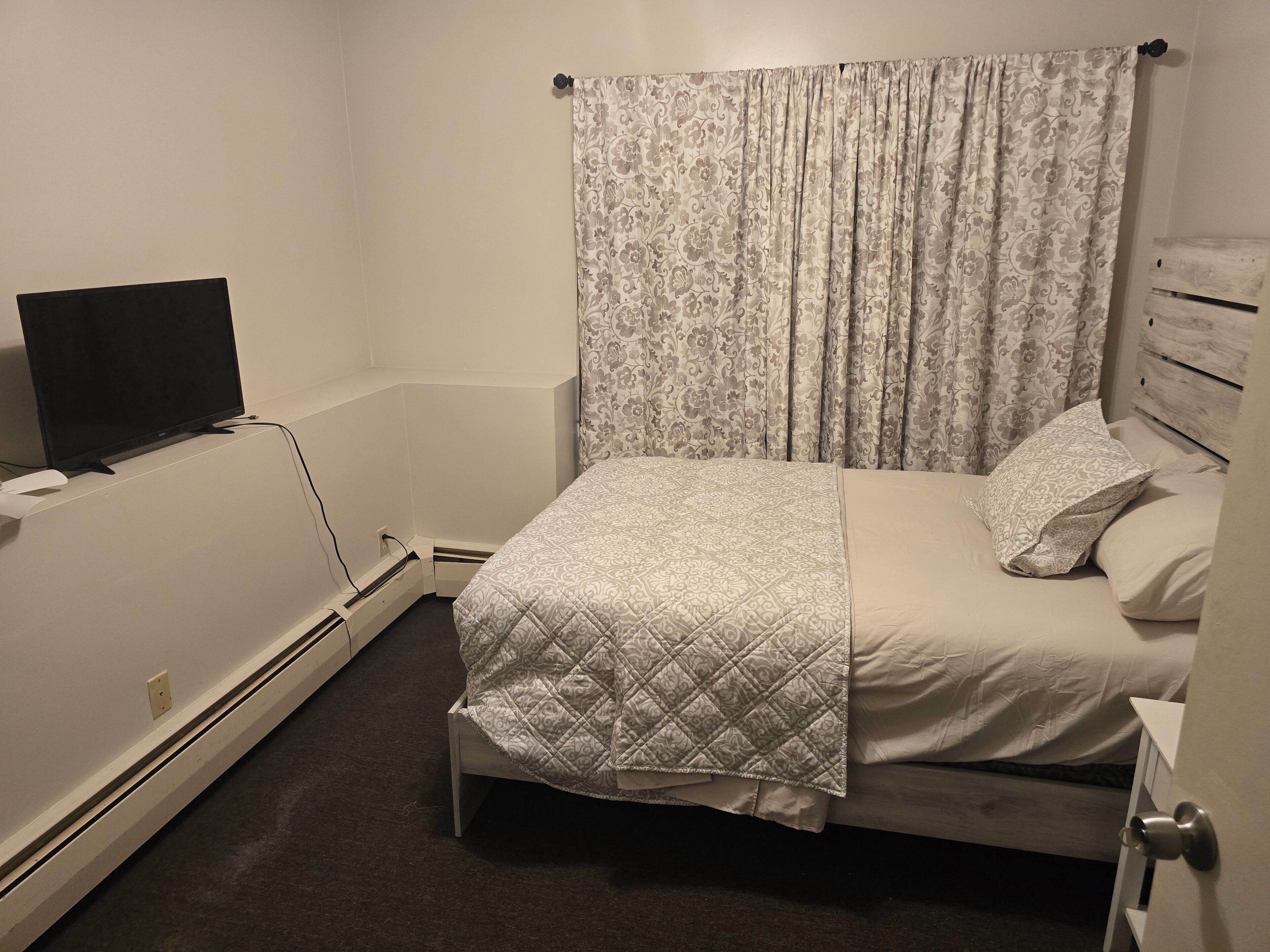 Een slaapkamer met een bed, een televisie en een raam met gordijnen.