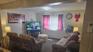 A living room with a television, sofas, a dining table, and a window with curtains.