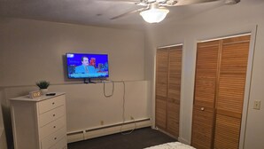 A bedroom with a bed, a dresser, a TV on the wall, and wooden closets.