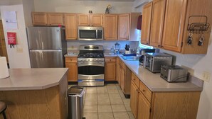 A kitchen with wooden cabinets, stainless steel appliances, a trash can, and a bar stool.