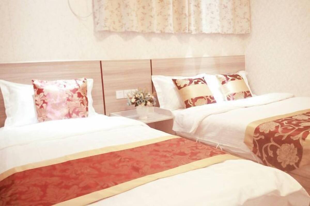 Une chambre d’hôtel avec deux lits, chacun agrémenté d’un oreiller à motifs floraux et d’une couvre-lit rouge et or. Une table de chevet avec un vase de fleurs se trouve entre les deux lits.