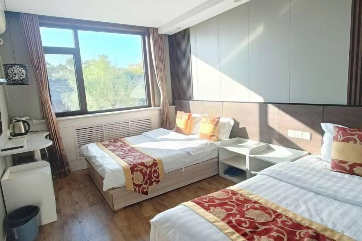 Une chambre d’hôtel avec un lit, un bureau, une chaise, une fenêtre et une vue sur les arbres.