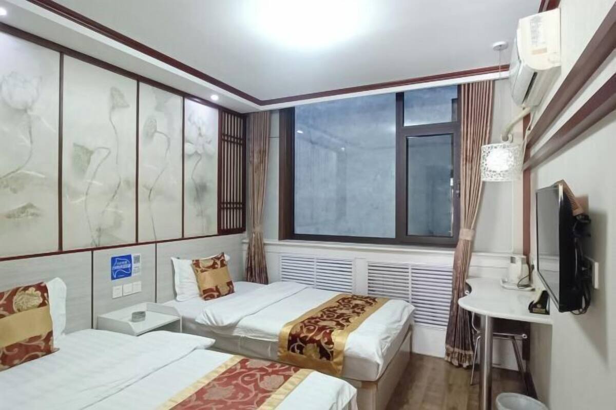 Une chambre d’hôtel avec deux lits, une petite table, un téléviseur et une fenêtre avec des rideaux.