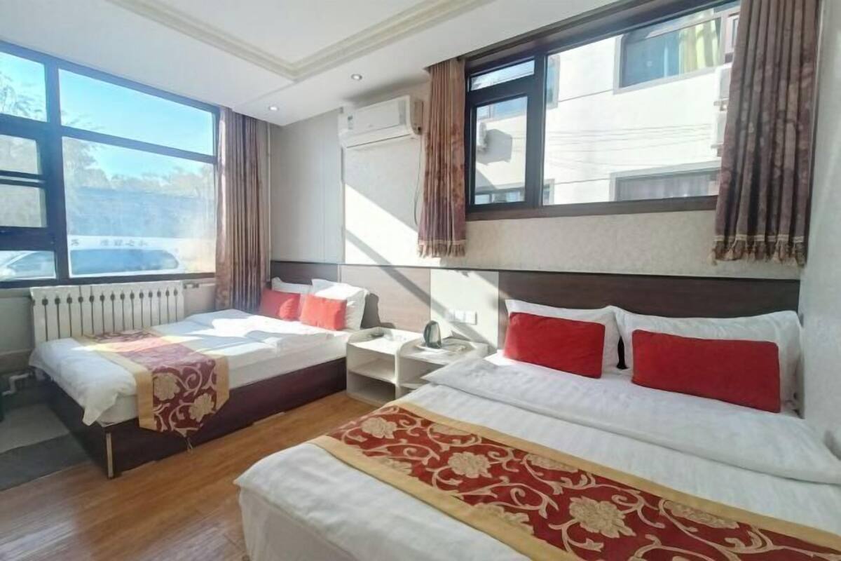 Une chambre d’hôtel avec deux lits, une fenêtre avec des rideaux, un radiateur et une table de chevet avec une lampe.