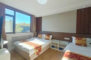 Hotellihuone, jossa on kaksi sänkyä, suuri ikkuna, televisio ja sisäänrakennettu hylly.