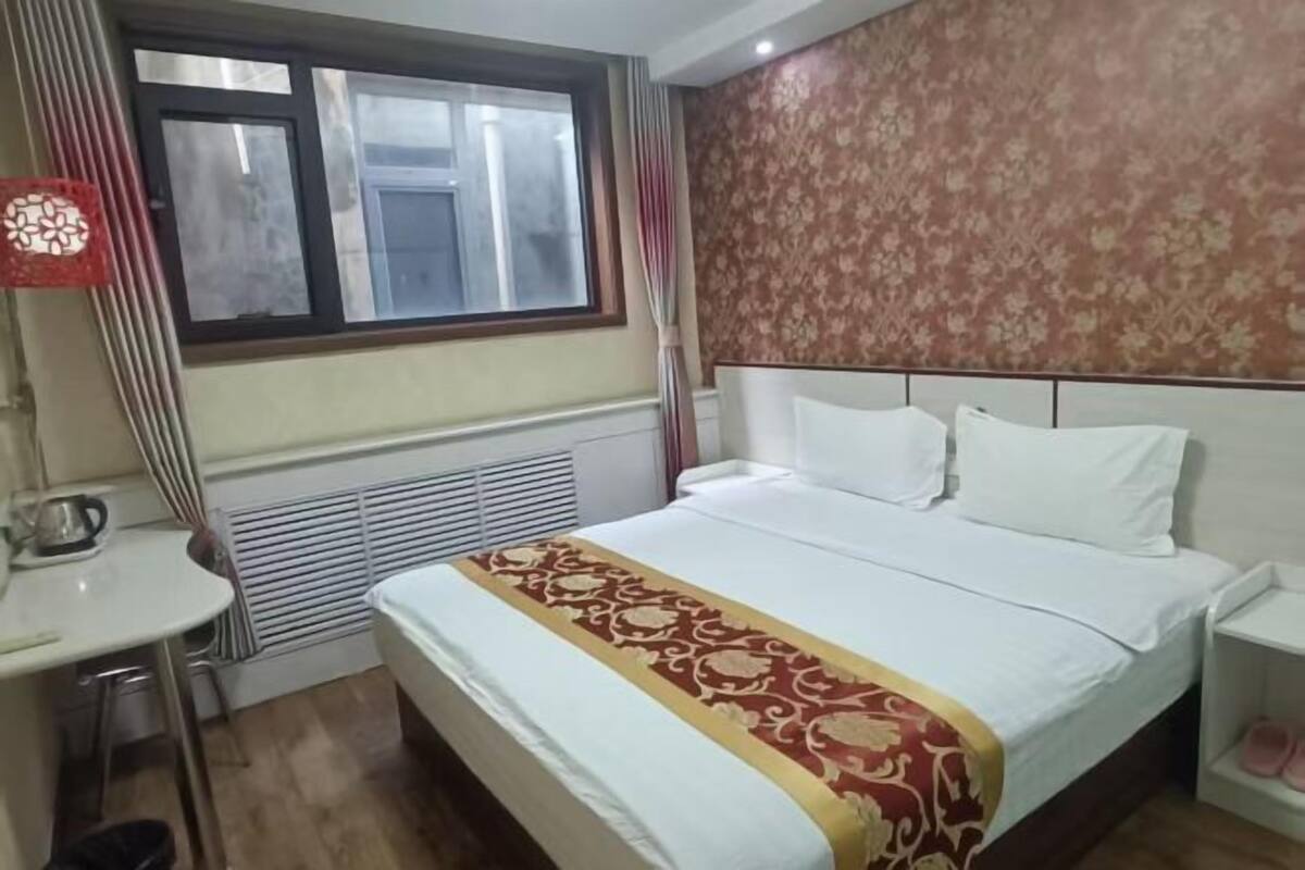 Une chambre d’hôtel avec un lit, un bureau, un radiateur, une fenêtre et un rideau.
