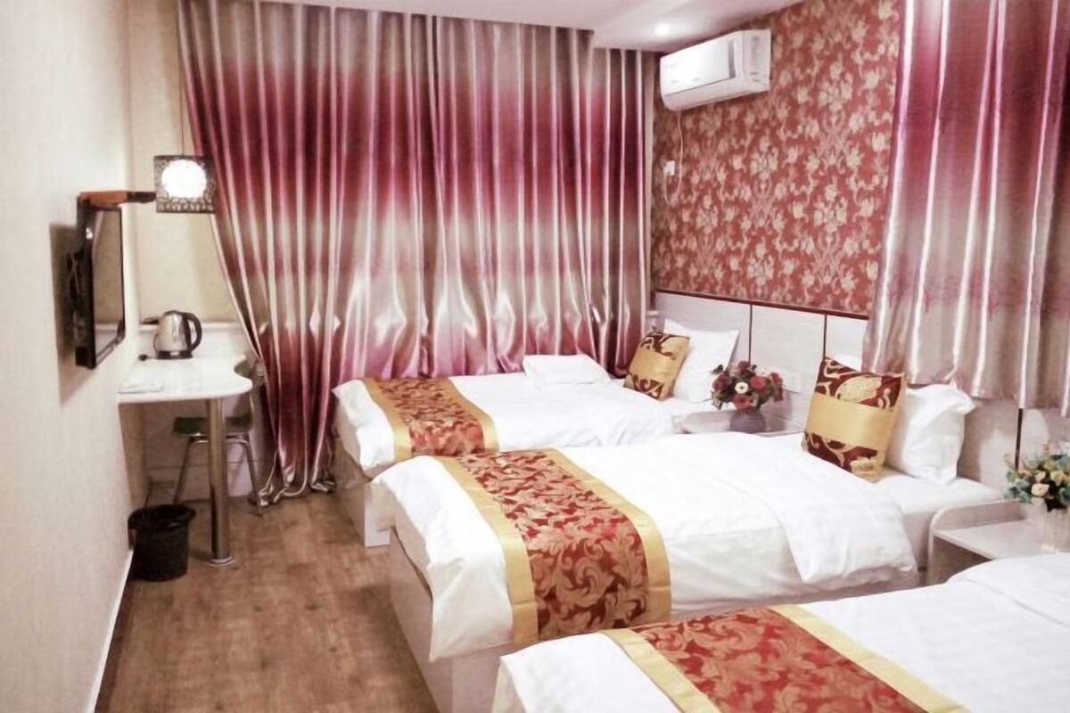 Une chambre d’hôtel avec deux lits, un bureau, une chaise, une poubelle et un climatiseur fixé au mur.
