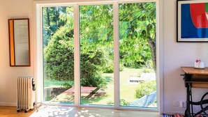 A room with a large sliding glass door leading to a garden, a radiator, a patterned rug, and a table with a small decorative item. - 4 Star Holiday Home in Frandefors (Frändefors)