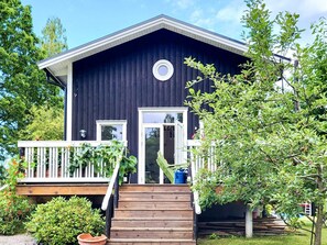 Une maison en bois sombre, avec un porche blanc, une porte d’entrée et une petite fenêtre ronde située au-dessus de la porte.