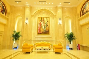A lobby with a large painting, a yellow sofa set, and two potted plants. - Vienna Hotel (Guangzhou)